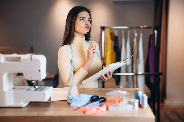 Mujer modista joven cose ropa en la máquina de coser. Crear y preguntarse sobre algo costurera en el taller. Creación de cursos de diseño de ropa en línea. — Foto de Stock