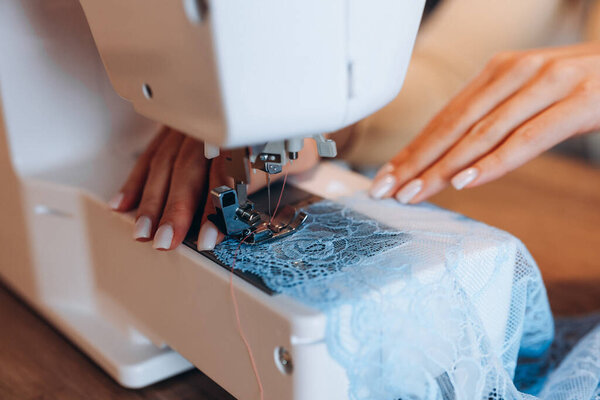 Close up young dressmaker woman working on sewing machine. Creating online clothing design courses.