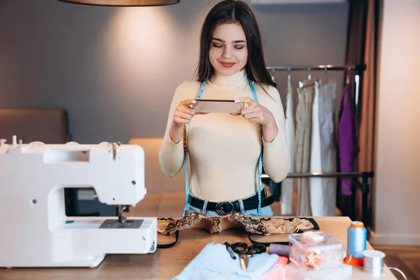 Mujer joven modista con máquina de coser. Costurera tomando una foto en el taller. Creación de cursos de diseño de ropa en línea. — Foto de Stock