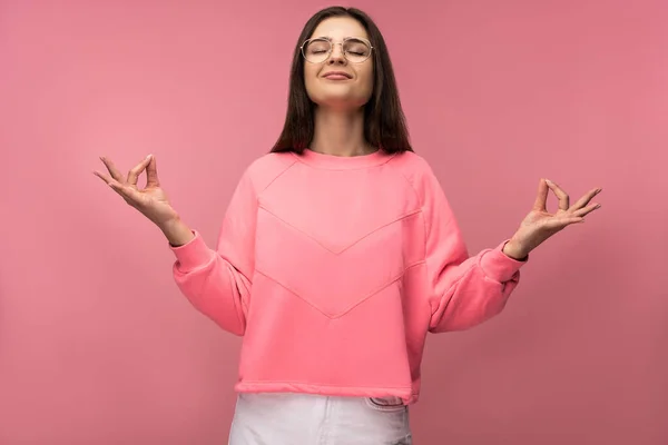 Фото привлекательной молодой женщины в очках, медитации и расслабления, носит случайные розовые футболки белые брюки изолированный розовый цвет фона — стоковое фото