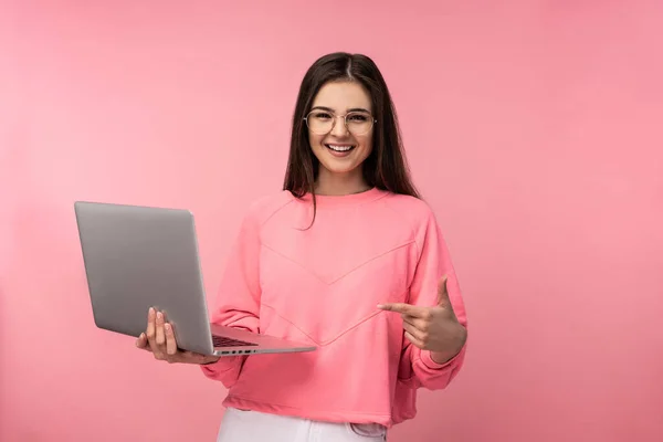 Фото привлекательной дамы в очках, улыбается и имеет онлайн встречу, держит ноутбук и работает в Интернете. носит случайные розовые футболки белые брюки изолированный розовый цвет фона. Онлайн-обучение. — стоковое фото