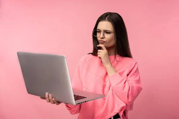 Фото привлекательной дамы в очках, заинтересованной и принимающей решение, держит ноутбук и работает онлайн. носить случайные розовые футболки белые брюки изолированный розовый цвет фона. — стоковое фото