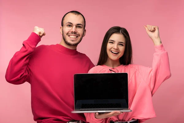 Photo of sweet couple holds laptop. Male and female look blessed and smile, isolated over pink background — Stock Photo, Image