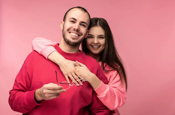 Photo of sweet couple, woman hug back her boyfriend. Male and female are in love look blessed and smile, isolated over pink background — Stock Photo, Image