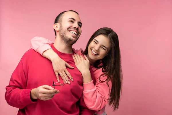 Photo of sweet couple hug each other and smile. Male and female are in love look blessed, isolated over pink background