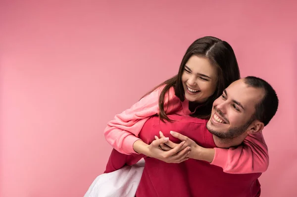 Photo of sweet couple hug each other and smile. Male and female are in love, isolated over pink background