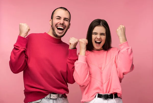 Photo of attractive man wih beard in red clothing and woman in pink smile and rejoice something. Couple looks funny, isolated over pink background — Stock Photo, Image