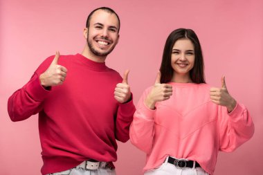 Kırmızı elbiseli çekici bir adam ve pembe elbiseli bir kadın baş parmağını kaldırır ve gülümser, pembe arka planda soyutlanır.