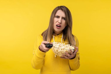 Çekici bir bayanın elinde televizyon kumandası ve bir tabak patlamış mısırla cansız bir yüz bir kanalı çevirmeye çalışıyor. Sıradan sarı kapüşonlu, izole sarı arka plan giyiyor.