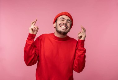 Sakallı, gözlüklü ve kırmızı elbiseli çekici bir adamın fotoğrafı. Erkek şans diliyor ve gülümsüyor, pembe arka planda izole edilmiş.