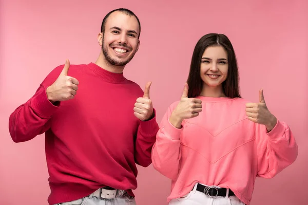 Фото привлекательного мужчины с бородой в красной одежде и женщины в розовой показать палец вверх и улыбку, изолированные на розовом фоне — стоковое фото