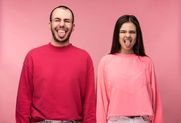 Photo of attractive man wih beard in red clothing and woman in pink grimace with tongue sticking out, isolated over pink background — Stock Photo, Image