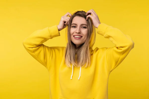 Foto de senhora atraente no capô posa de uma forma fofa. Usa casual amarelo com capuz, isolado cor amarela fundo — Fotografia de Stock