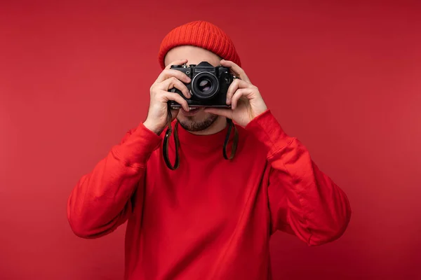 Fénykép a vonzó férfi szakállas szemüveg és piros ruhát. Happy férfi tartja kamera és képeket készít, elszigetelt piros háttér — Stock Fotó