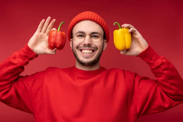 Foto van een aantrekkelijke man met baard in bril en rode kleding. man houdt papieren in handen, toont liefde voor groenten geïsoleerd over rode achtergrond — Stockfoto