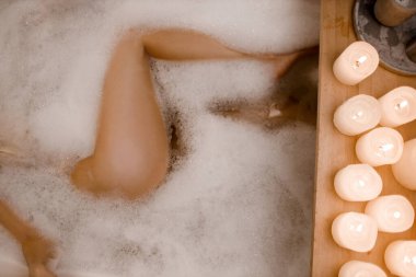 Kadınların spa küvetindeki, köpüklü, ahşap masa vazosundaki bitki mumlarıyla çekilmiş bacaklarını yakın plan çek. Modern spa merkezi