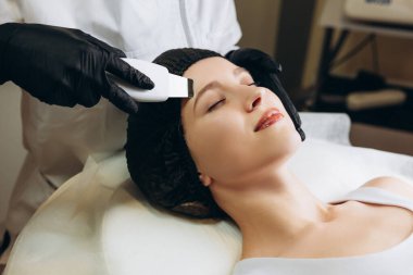 Güzellik salonunda, kozmetolojide ve yaşlanma karşıtı fotoğraflarda yüz gençleştirme için makine kozmetoloji prosedürü uygulayan genç bir kadın.