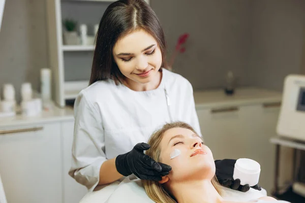 Kozmetik uzmanı, müşterinin cildini geliştirmek için yüz yüzeyine krem özü vitaminleri uyguluyor. Güzellik uzmanı hasta için güzellik tedavisi yapıyor. Sağlık, cilt bakımı, estetik tıp konsepti