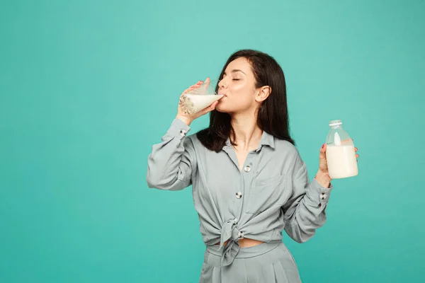 Çekici bir kadının fotoğrafı süt ve süt ürünleri içiyor. Gri gömlek giyer, izole turkuaz renk arkaplan