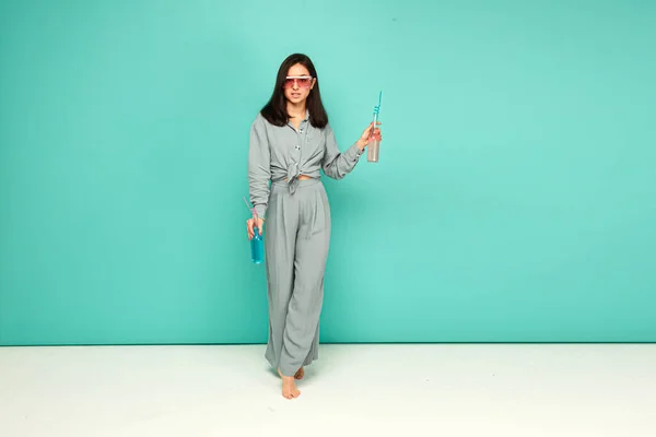 La foto de la señora atractiva en las gafas de sol bebe los cocteles, el verano. Lleva camisa gris, fondo de color turquesa aislado. —  Fotos de Stock