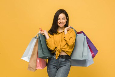 Genç bir bayanın konsept fotoğrafı, alışveriş torbaları, giysiler. Sarı gömlek giyiyor, izole edilmiş sarı arkaplan