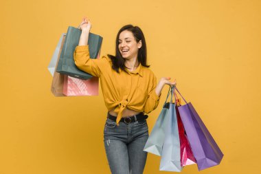 Genç bir bayanın konsept fotoğrafı, alışveriş torbaları, giysiler. Sarı gömlek giyiyor, izole edilmiş sarı arkaplan