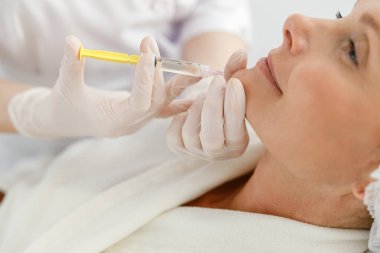 Yakın çekim yaşlı bir kadına mezoterapi iğnesi yapar. Yüzündeki kırışıklıkları sıkılaştırdığı ve düzelttiği için bir güzellik uzmanı tarafından tedavi edilen bir kadın.