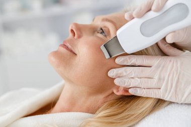 Ultrasonik yüz temizleme işlemi sırasında profesyonel güzellik salonundaki son sınıf kadınını kapat. Yüz bakımı, yüz temizliği.