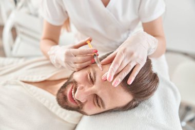 Yakın çekim genç adama mezoterapi iğnesi yapar. Bir güzellik uzmanının cilt kırışıklıklarını düzeltmesi ve düzeltmesi için erkeğe uyguladığı tedavi.