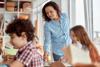 Genç öğretmen öğrencisini okumaya yardım eder. İlkokul çocukları sıralarında oturup sınıfta kitap okuyorlar.