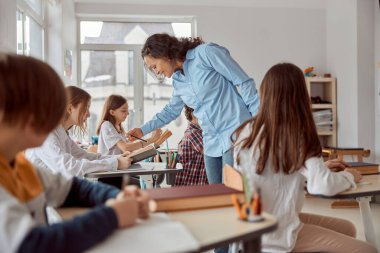 Tatlı öğretmen öğrencisini okumaya yardım eder. İlkokul çocukları sıralarında oturup sınıfta kitap okuyorlar.