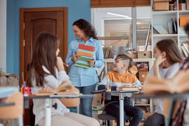 İlkokul öğretmeni sınıfta duruyor. Öğrenciler sıralarında otururken bayan öğretmen derse başlayacak.