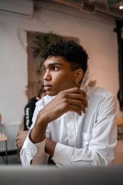 A young black man is sitting at the table with a laptop, drinking tea and using a smartphone. The guy in the cafe. Work outside the office, remote work or study concept.