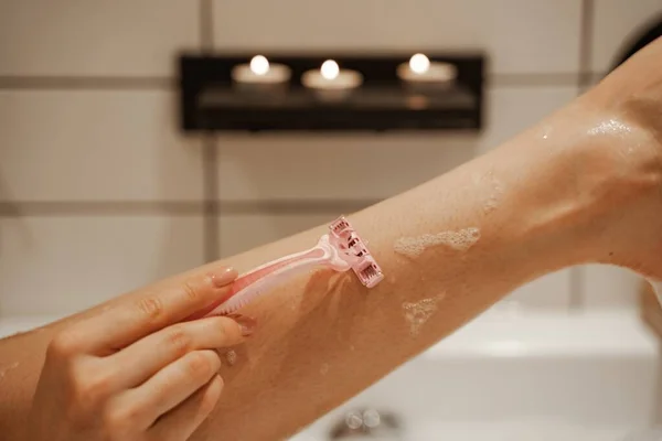 Nahaufnahme junge Frau rasiert sich mit Rasiermesser ihr Bein in der gemütlichen Badewanne voller Schaum und dekoriert mit Kerzen. Gesunde Behandlung und Genuss — Stockfoto