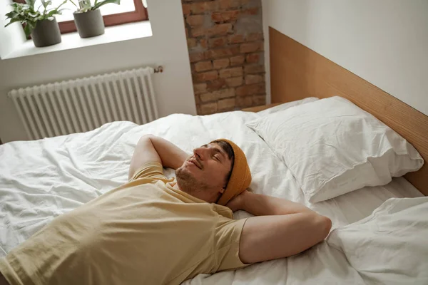Hombre joven viajero está acostado en la cama en la habitación de hotel en las vacaciones de verano. Hombre fresco en ropa casual — Foto de Stock