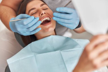 Neşeli dişçi ve dişçi müşterisi. Diş tedavisinde kadın hasta, modern diş kliniğinde diş aletleri kullanan doktor.