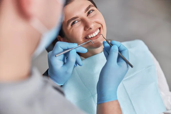 Neşeli dişçi ve dişçi müşterisi. Diş tedavisinde kadın hasta, modern diş kliniğinde diş aletleri kullanan doktor..