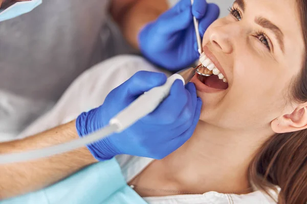 Mulher bonita sentada na cadeira dental, enquanto médico profissional fixando os dentes — Fotografia de Stock
