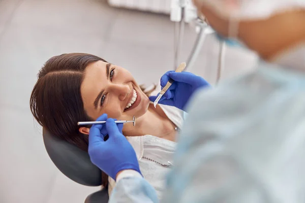 Retrato de jovem dentista em luvas examinando dentes de cliente feminino no hospital — Fotografia de Stock