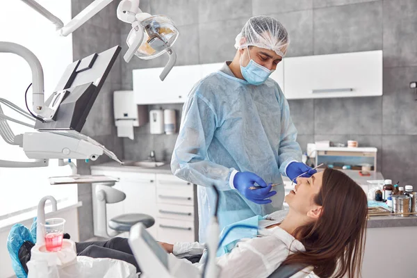 Allegro dentista positivo e cliente in odontoiatria. Si guardano e sorridono. cliente femminile sedersi in sedia — Foto Stock