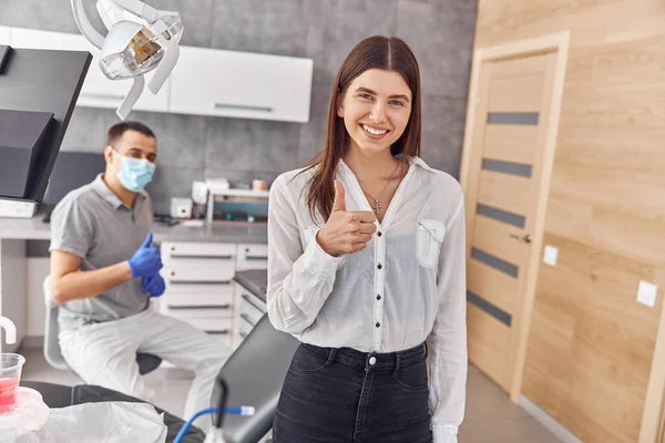 Imagem de uma bela jovem cliente feliz do sexo feminino dando polegares no escritório do dentista. — Fotografia de Stock