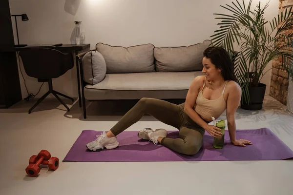 Una joven entrena con pesas y una esterilla de yoga. Entrenamiento en casa. Deportes y vida cotidiana — Foto de Stock