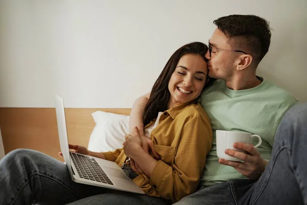 Hermosa pareja viendo películas con sentimientos románticos, sentada en la cama con café. Familia feliz mudándose a nuevo apartamento — Foto de Stock