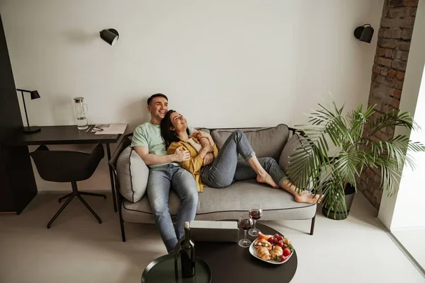 Preciosa pareja joven mostrando sentimiento romántico el uno al otro sentado en el sofá en la sala de estar. Familia feliz mudándose a nuevo apartamento — Foto de Stock