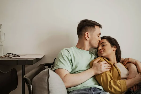 Υπέροχο νεαρό ζευγάρι που δείχνει ρομαντικό συναίσθημα ο ένας στον άλλο καθισμένο στον καναπέ. Ευτυχισμένη οικογένεια μετακομίζει σε νέο διαμέρισμα — Φωτογραφία Αρχείου