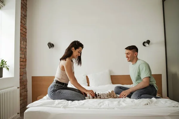 Um jovem casal feliz está a passar o tempo livre a jogar xadrez. Jovem família se mudando para novo apartamento — Fotografia de Stock