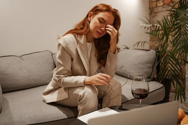 Egy fiatal, vörös hajú nőnek fáj a feje és fáj a szeme a laptopnál töltött kemény nap után. Száraz szemek és stressz. üzleti út turizmus a szállodában. — Stock Fotó