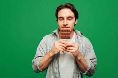 Genç adam yeşil arka planda izole edilmiş çikolata kokusundan hoşlanıyor.