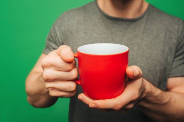 Yakından bir fincan çay tutuyor, yeşil arka planda izole edilmiş.