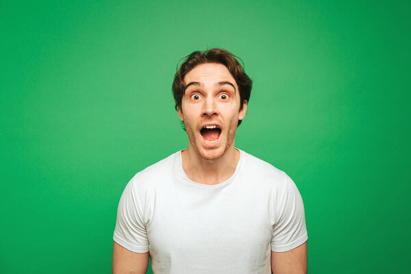 Молодой человек выглядит удивленным новостями, изолированным на зеленом фоне